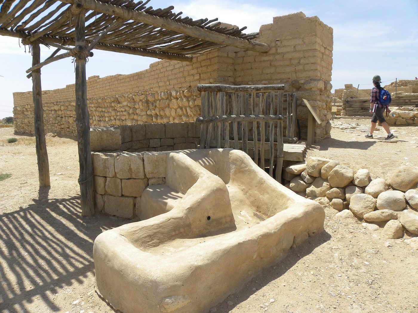 Stone well and trough beside the outer gate at Tel Be'er Sheva, with excavated walls and dry Negev ground around it.