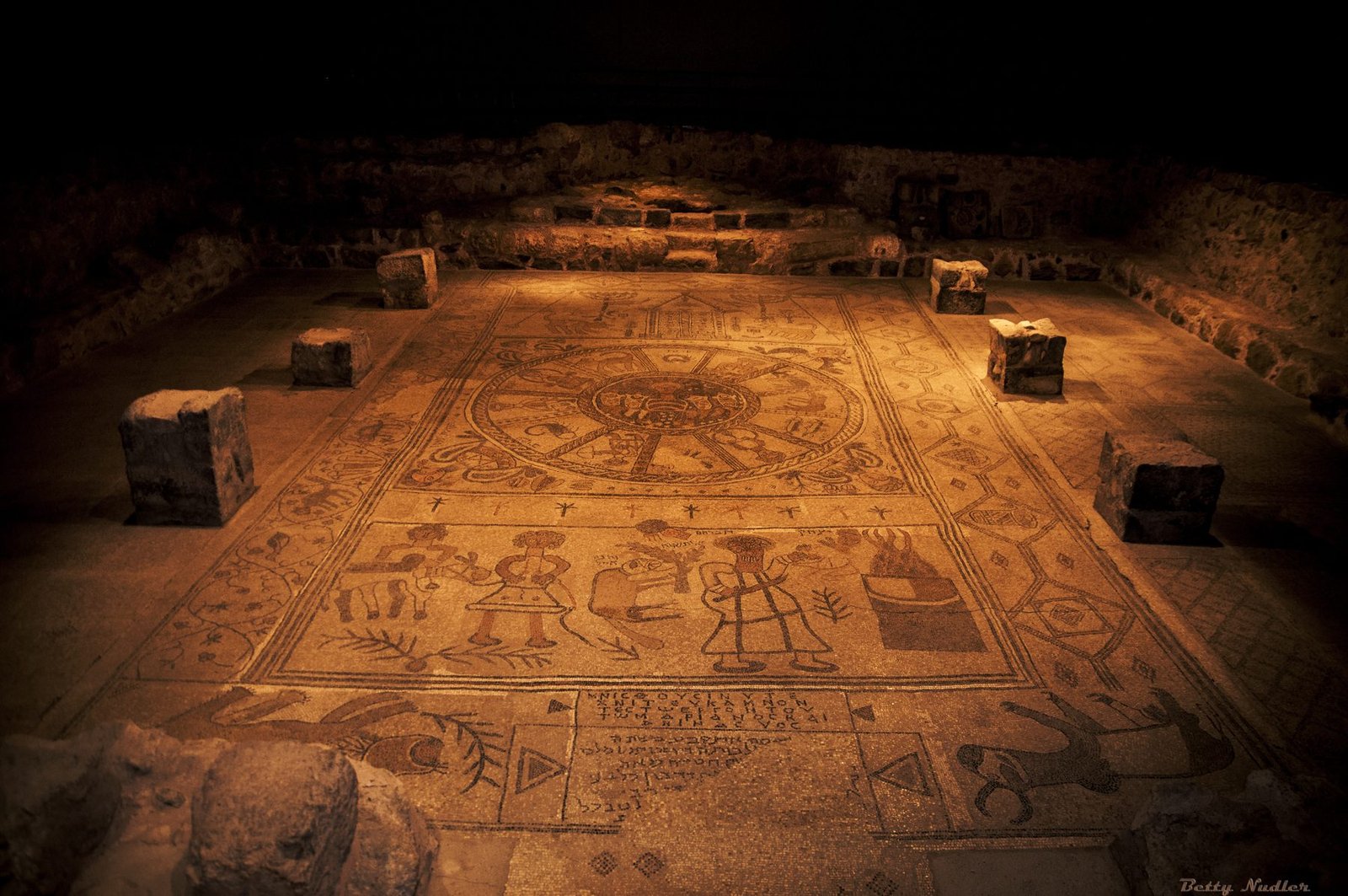 The Beit Alpha synagogue mosaic floor seen in situ, three panels stacked: the Torah ark, the central zodiac wheel with Helios, and the Binding of Isaac