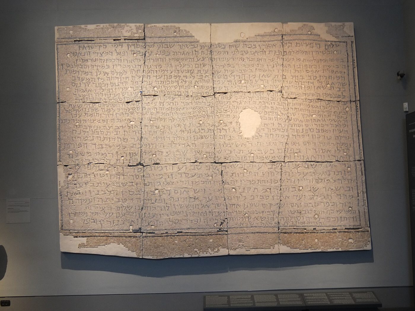 Large stone panel of the Mosaic of Rehob displayed on a museum wall, covered with lines of Hebrew inscription.
