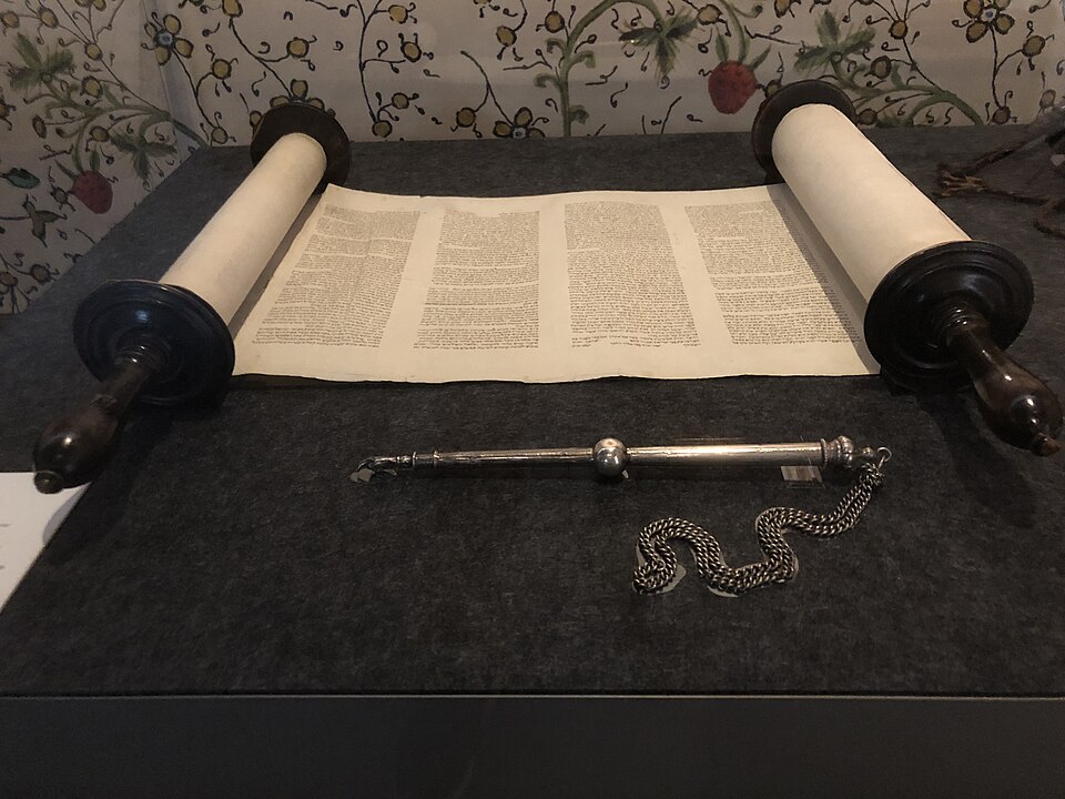 An open Torah scroll on wooden rollers with a silver yad pointer and chain laid in front